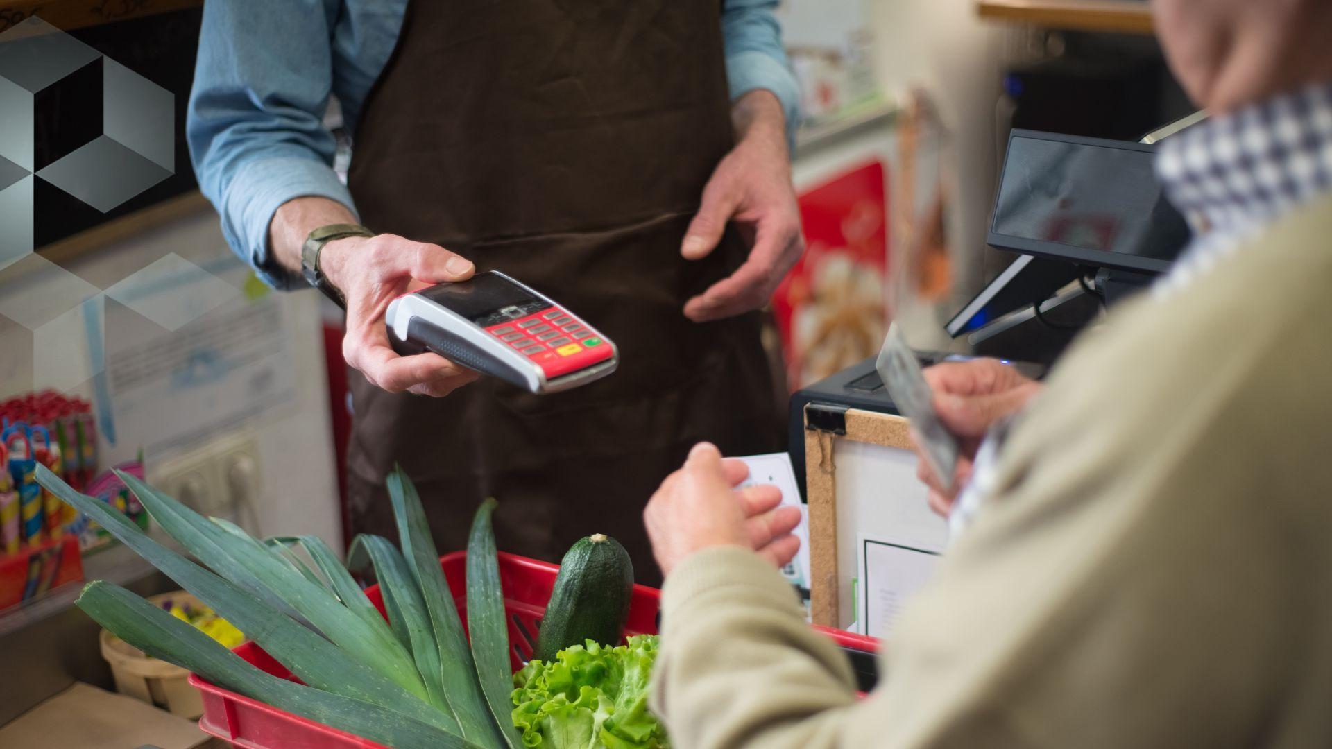 A person holds out a card machine for another person to pay for groceries